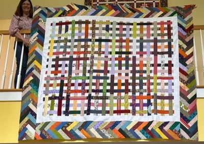 Person holding a colorful patchwork quilt with various patterns.