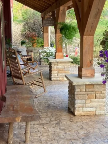 Cozy porch with rocking chairs, stone pillars, and potted plants.