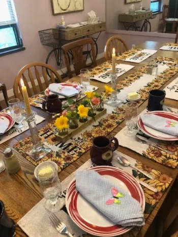 Dining table set for a meal with floral centerpiece, plates, cups, and lit candles.