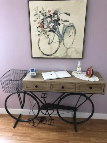 A desk designed to resemble a bicycle under a painting of a bike, with items on top.