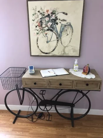 A desk designed to resemble a bicycle under a painting of a bike, with items on top.