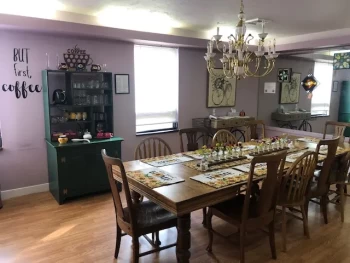 Dining room with wooden table, chairs, chandelier, and a coffee station with a "But first, coffee" sign.